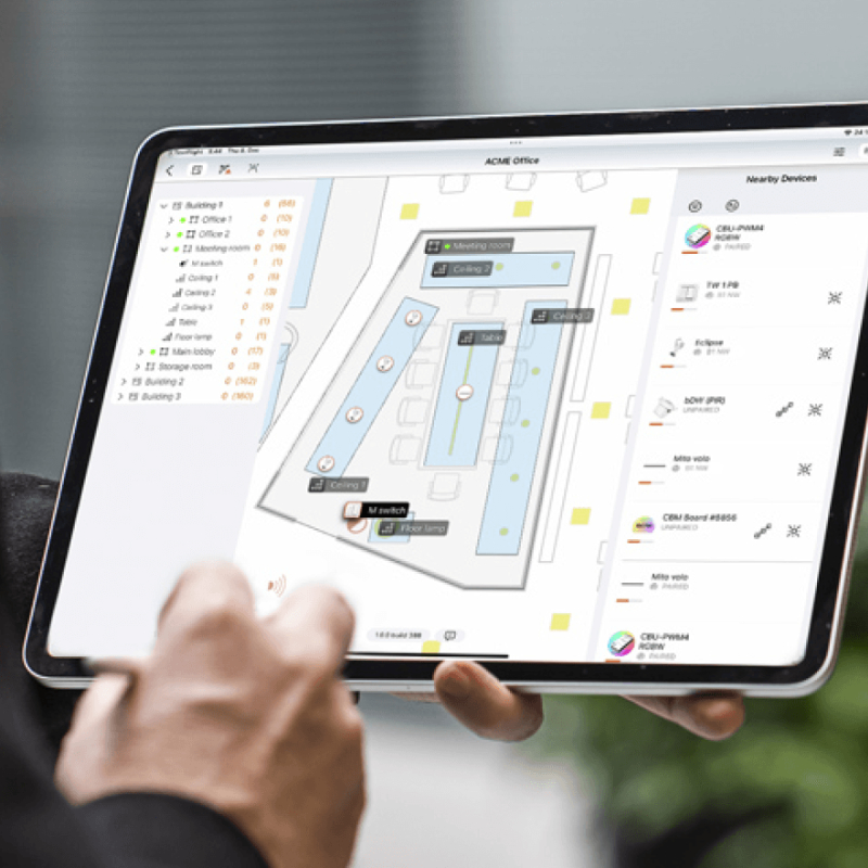 A technician using a tablet interface to configure and commission a smart wireless lighting control network on an office floor plan.